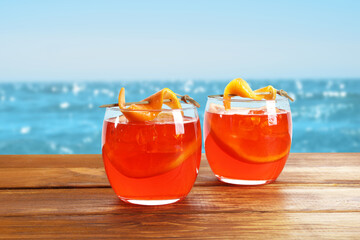Aperol spritz cocktail with orange slices on wooden table at beach