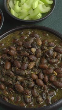 Black soybean curry. Pickled chilies and celery stalks on the side. Spinning left and right - seamless loop. Vertical video.