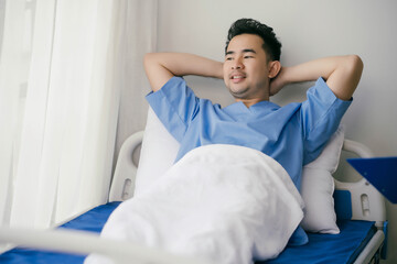 A man in a blue hospital gown is laying in bed with his arms crossed