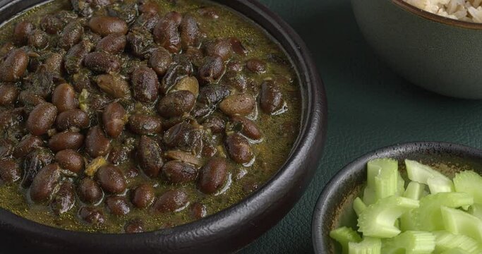 Black soybeans cooked in spices. Bhat ki Chudkani - a traditional dish of the Kumaon region. Celery stalks, pickled chilies, and brown basmati rice on the side. Table spin. 