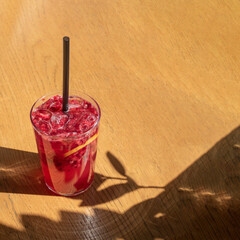Raspberry iced tea cocktail on a wooden table with sunshade spring creative concept with copy space. 