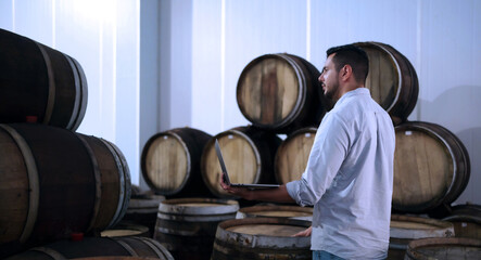 Professional man winemaker or owner working and inspecting wine quality in wine cellar with wooden barrel in wine factory. Winery manufacturing industry, Alcohol and winemaking fermentation process.