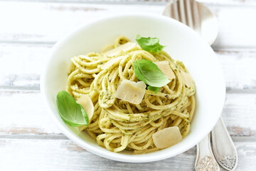 Spaghetti with olive pesto sauce and fresh basil. Bright wooden background. Close up