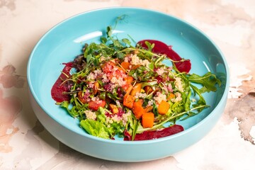 Colorful salad with pumpkin, lettuce, tomatoes, and quinoa on a blue plate
