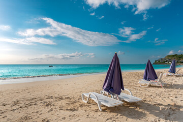 Fototapeta na wymiar Relaxing beach chairs with umbrellas on a tropical white sand beach in the Caribbean overlooking clear turquoise waters