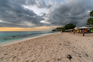 A colorful cafe on the sand on the Caribbean island of Antigua with turquoise waters and storm clouds at dusk