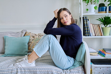 Young sad unhappy woman sitting on couch at home