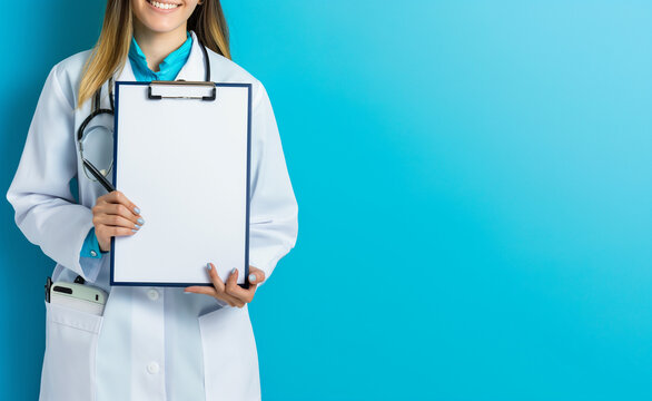 A female doctor in a white coat holds a clipboard against a blue background.