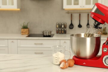 Modern red stand mixer, eggs and container with flour on white marble table in kitchen, space for text