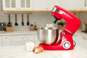 Modern red stand mixer, eggs and container with flour on white marble table in kitchen