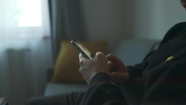 Man hands using smartphone in home interior while sitting on the sofa in modern design interior, cheerful hipster guy typing an sms message at social network. High quality FullHD footage