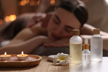 Spa therapy. Beautiful young woman lying on table during massage in salon, focus on burning candles and cosmetic products