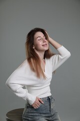 Beautiful young woman sitting on stool against grey background