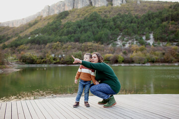 A happy mother holds a four-years-old child in his arms against the background of a lake, forest and mountain