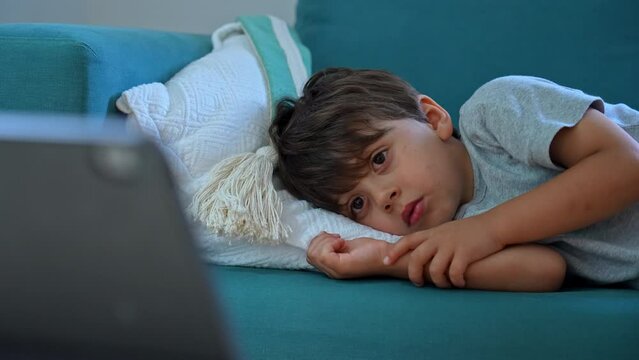 Digital Engagement - Young Boy’s Focused Attention On Tablet Screen In Close-Up. Child Watching Cartoons Online Laid On Sofa Couch At Home