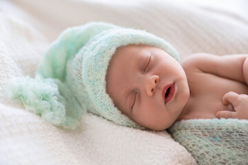 Cute newborn baby in warm hat sleeping on white plaid, closeup