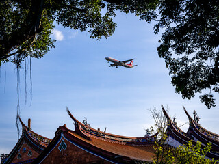 An airliner  flies over the Confucius Temple in Taipei before landing at Songshan Airport on a summer afternoon, creating a vivid contrast between tradition and modernity.