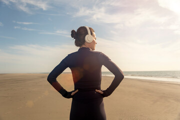 Rear view of a sporty woman with her hands on her hips resting after exercise at the beach