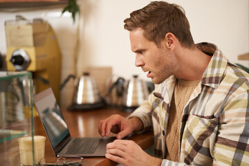 Portrait of man looks frustrated at laptop screen, staring at monitor with shocked face expression,...