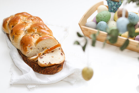 Cutted easter loaf bread on wooden plate on white table, blurry background with easter decoration