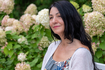 Serenely poised against a garden, flower, backdrop, a woman exudes confidence and contentment,...