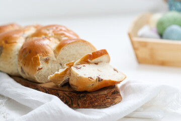 Cutted easter loaf bread on wooden plate on white table, blurry background with easter decoration