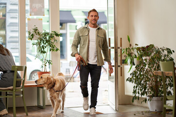 Portrait of handsome young man walks into the cafe with his dog on a leash, enters pet-friendly...