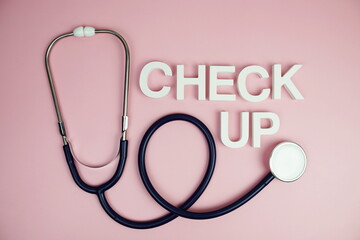 Stethoscope and Check up alphabet letters top view on pink background