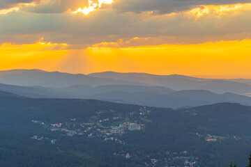 Krajobraz ze szczytu Skalny Stół w letniej odsłonie z widokiem na miasto Karpacz i całe Karkonosze o zachodzie słońca.
