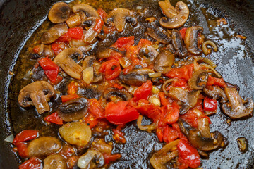 Champignon with tomato and onion is stewed in a frying pan