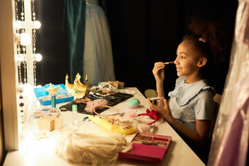 Side view portrait of smiling Black girl doing makeup and looking into mirror backstage preparing...
