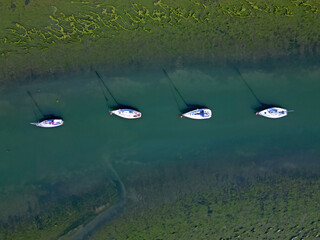 Four sailing boats mooring in nature reserve. A natural harbor in salty marsh in Keyhaven, Hampshire, UK. Beautiful sea colors from blue to green and abstract algae pattern.