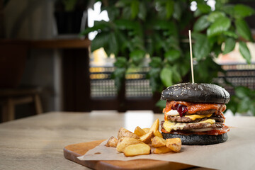 delicious fresh black burger with cheese and tomato sauce serving with french fries on a wooden...