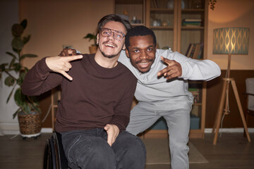 Front view portrait of young man with disability posing with African American friend during house...