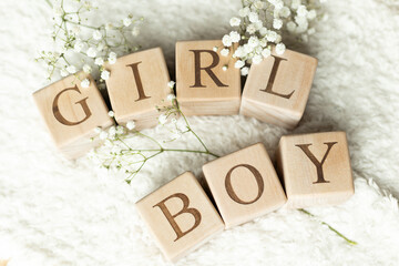 Wooden blocks spelling out the words GIRL and BOY lying flat on a white, fluffy blanket with white...
