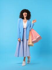 Happy young woman with shopping bags on light blue background. Space for text