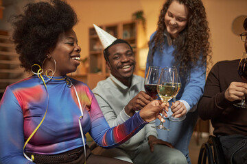 Side view portrait of Black young woman clinking glasses with diverse group of friends during party celebration at home