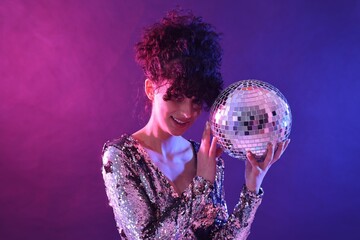 Beautiful young woman with disco ball posing on color background in neon lights