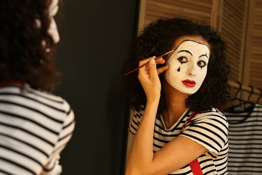 Young woman applying mime makeup near mirror indoors