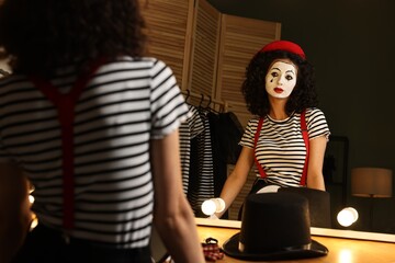 Young woman in mime costume posing near mirror indoors