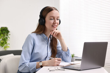 E-learning. Young woman using laptop during online lesson at white table indoors