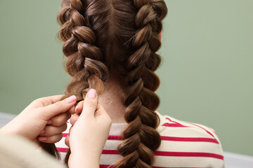 Professional stylist braiding woman's hair on olive background, closeup