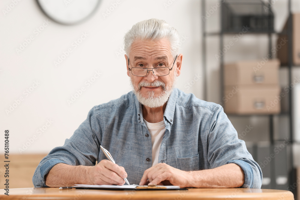 Sticker Senior man signing Last Will and Testament at table indoors