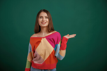 Showing by hand to the side, place for text. Young woman is standing against green background in the studio