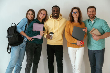 Holding notepads and coffee cup. Group of young people are standing against white background - 765110825
