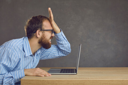 Argh, don't remember it. Side profile view angry ashamed guy slaps face sitting at office desk with laptop. Businessman makes stupid mistake online, forgets password, fails to fix computer malfunction