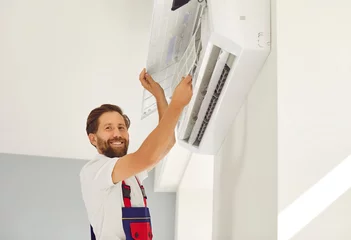  Portrait of smiling male technician in work uniform installing or repairing air conditioner. Technician is installing air conditioning equipment with screwdriver. Concept of technician service. © Studio Romantic
