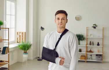 Portrait of a young smiling man standing at home or in hospital on rehabilitation with his arm in a...