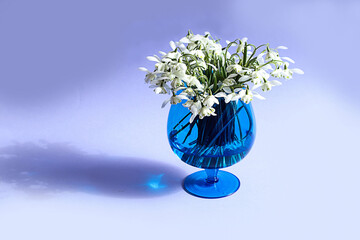 Spring mood: a bouquet of snowdrops in a blue vase on a blue background