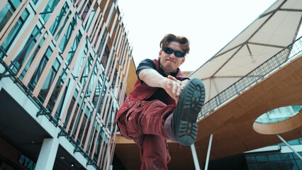 Low angle of asian attractive hipster pose at camera surround by mall. Portrait of break dance choreographer looking at camera while dancing in hip hop style. Outdoor sport 2024. Endeavor. - obrazy, fototapety, plakaty